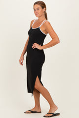 woman wearing a black midi dress with white straps and a side slit, standing in profile with flip flops