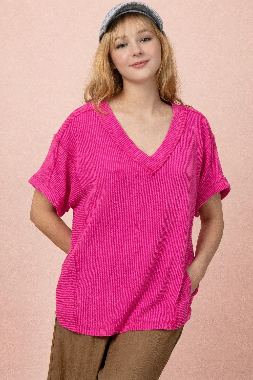 woman wearing a bright pink oversized v-neck knit top with short sleeves and front pockets