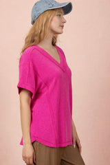 woman wearing a bright pink short sleeve v-neck knit top with a relaxed fit and side slits