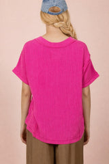 woman wearing a vibrant pink oversized knit top with short sleeves and a relaxed fit, viewed from the back