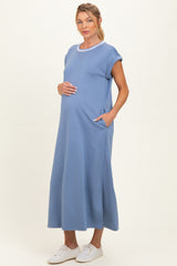 woman wearing a light blue maternity dress with short sleeves and pockets, gently cradling her baby bump