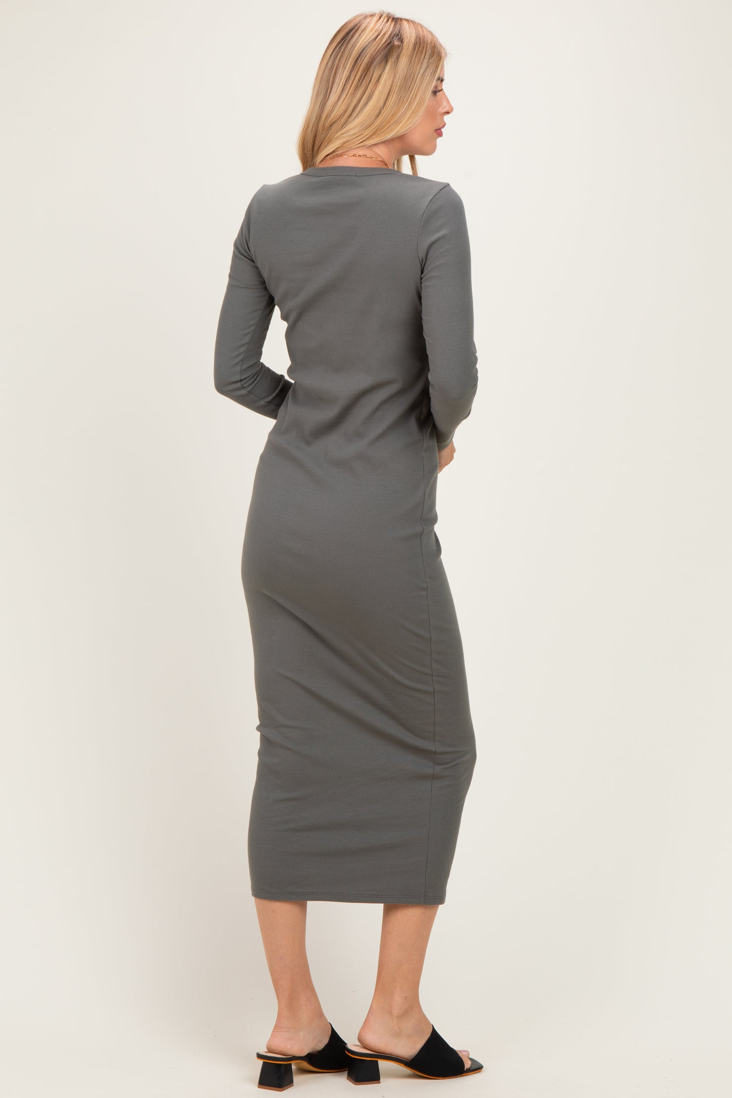 woman wearing a fitted gray long sleeve maxi dress, view from the back, paired with black slide sandals