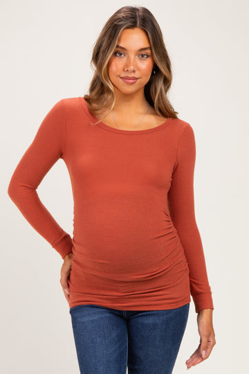 woman wearing a rust long sleeve maternity top with ruching at the sides and a visible baby bump