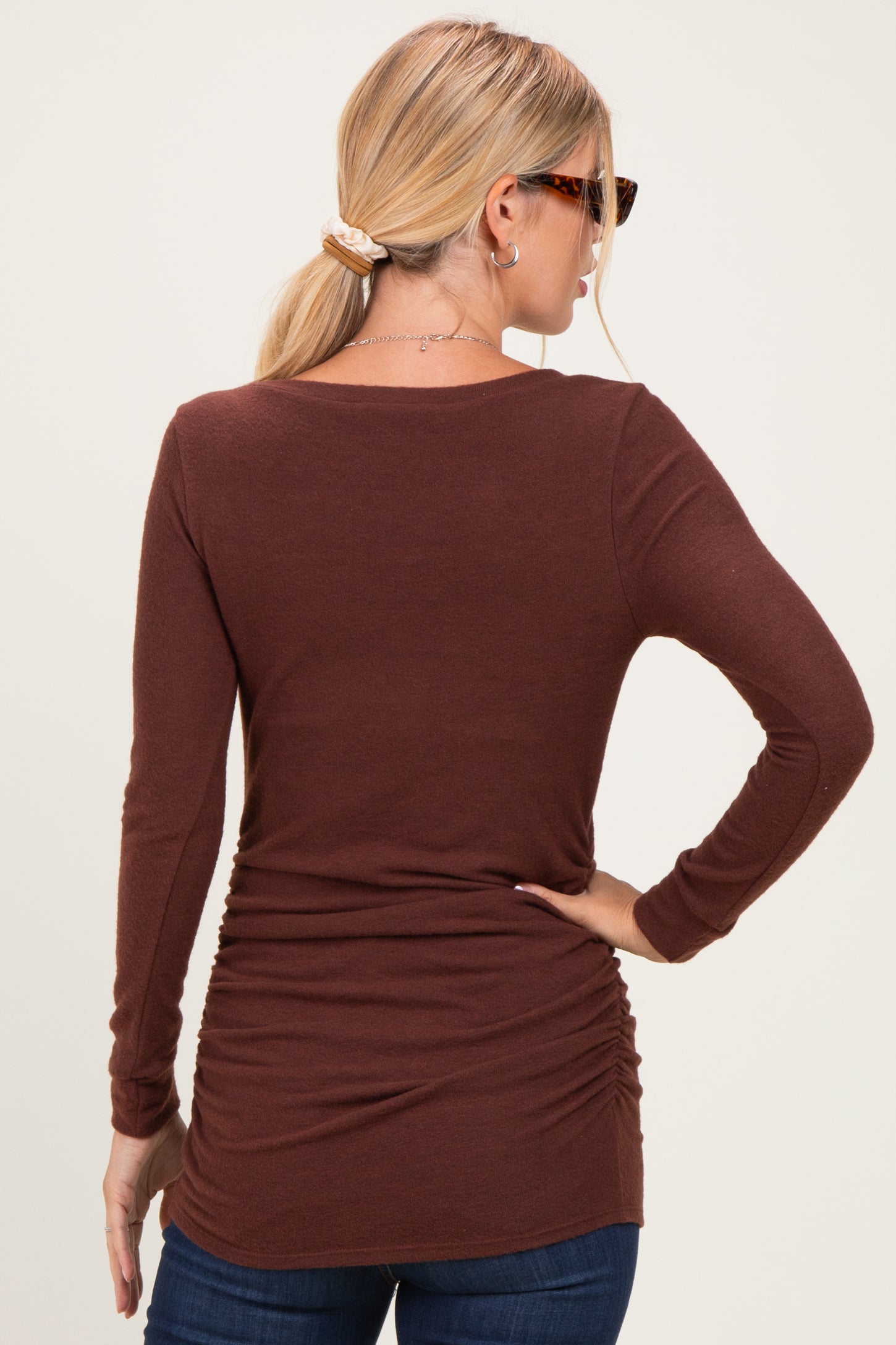 woman wearing a brown long sleeve top with gathered detailing at the back, styled with jeans and sunglasses