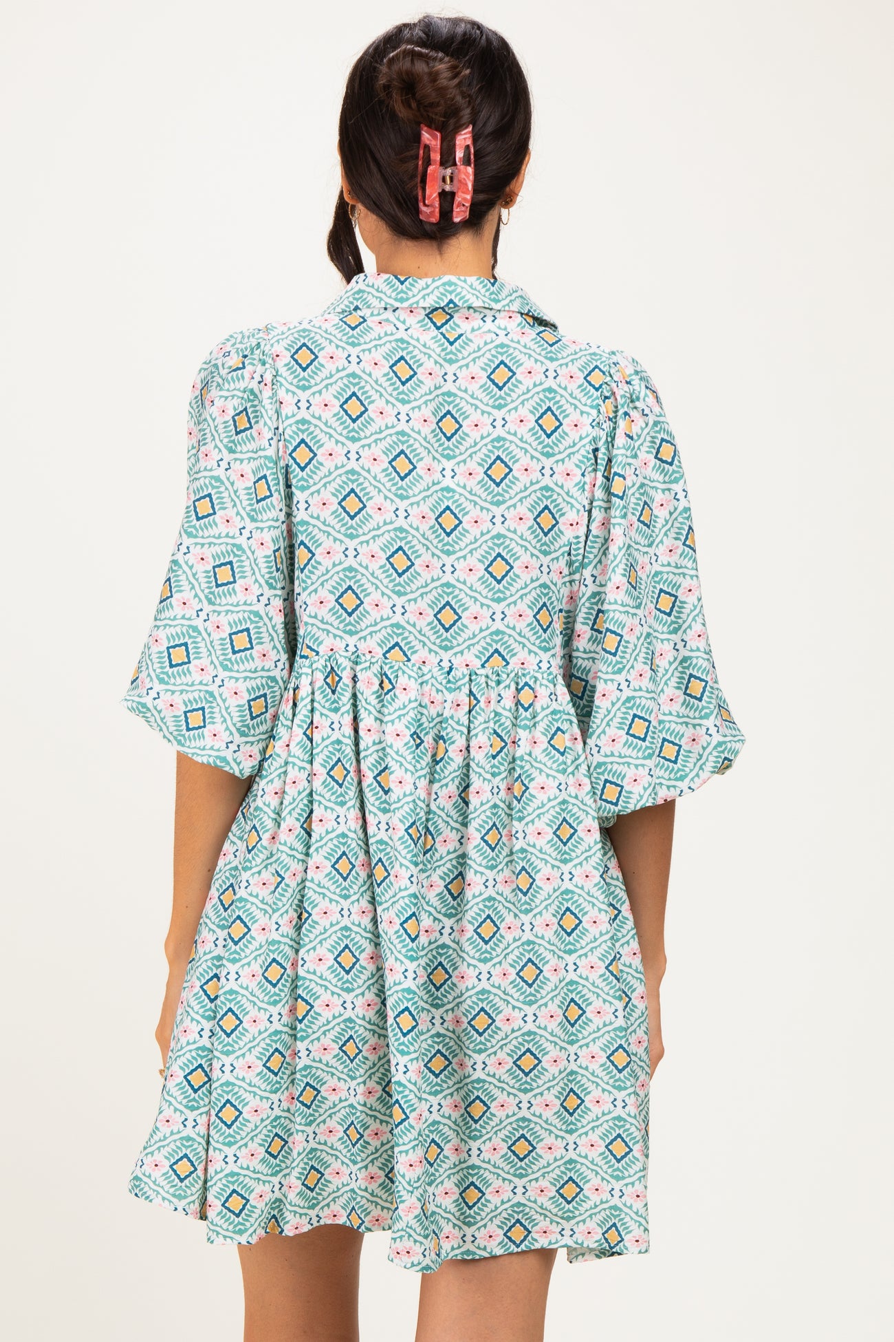 woman wearing a short-sleeve teal patterned dress with a gathered waist and a collar, seen from the back