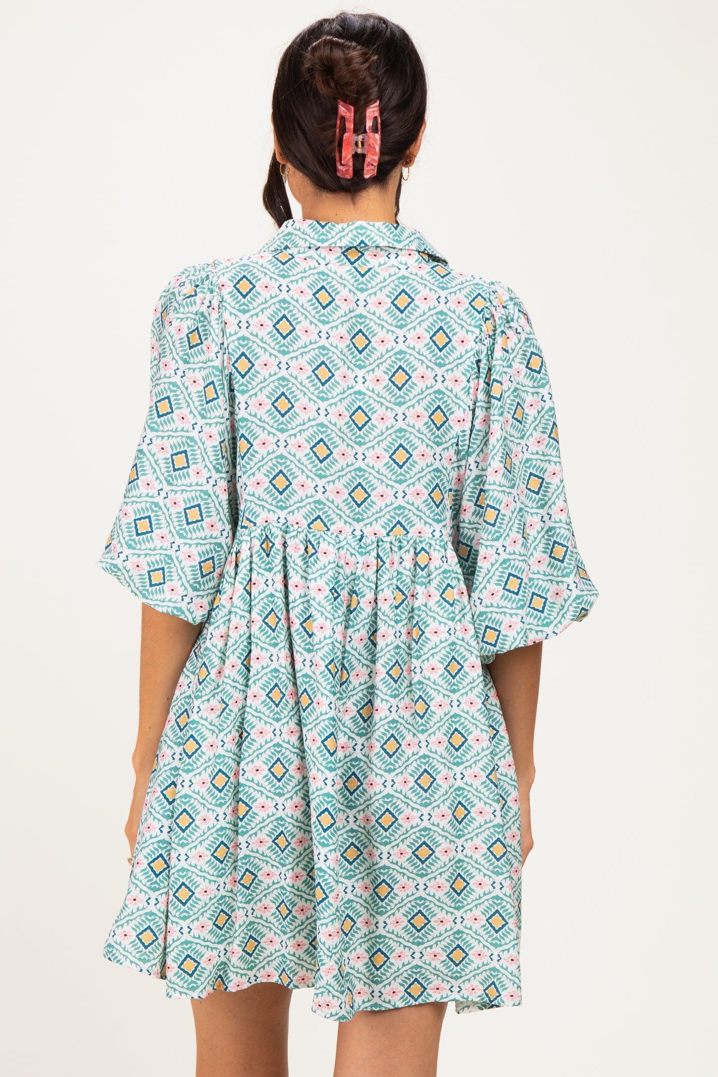 woman wearing a short-sleeve teal patterned dress with a gathered waist and a collar, seen from the back