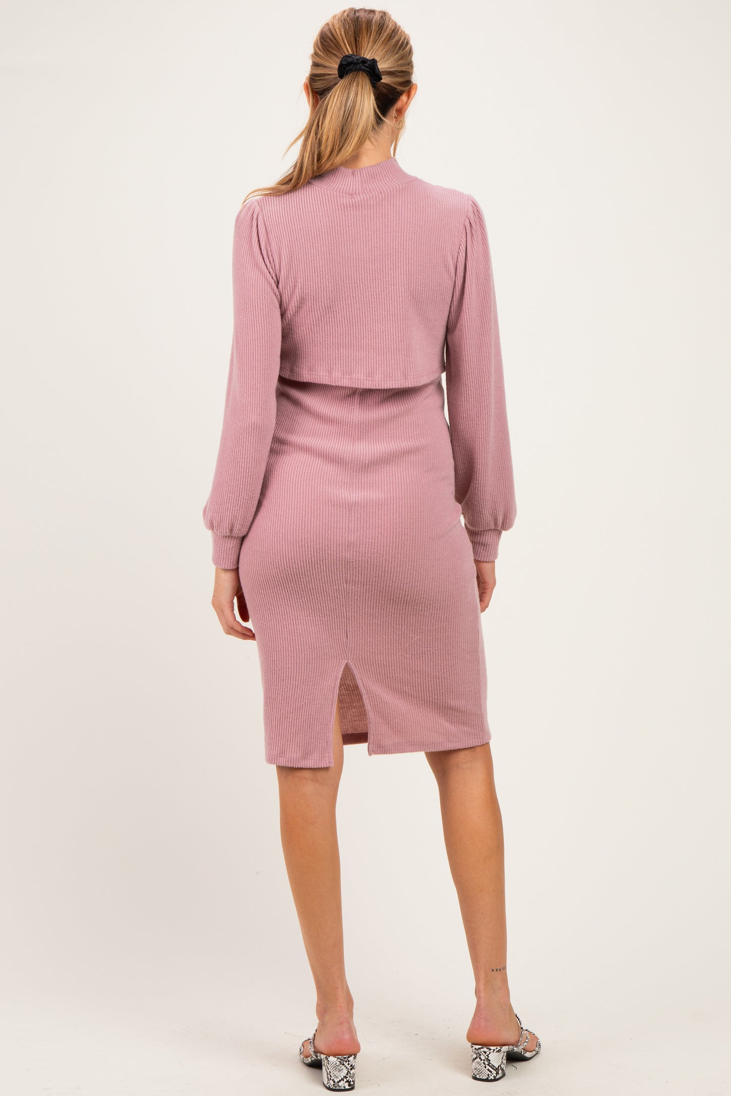 woman wearing a pink ribbed maternity dress with long sleeves and a back slit detail