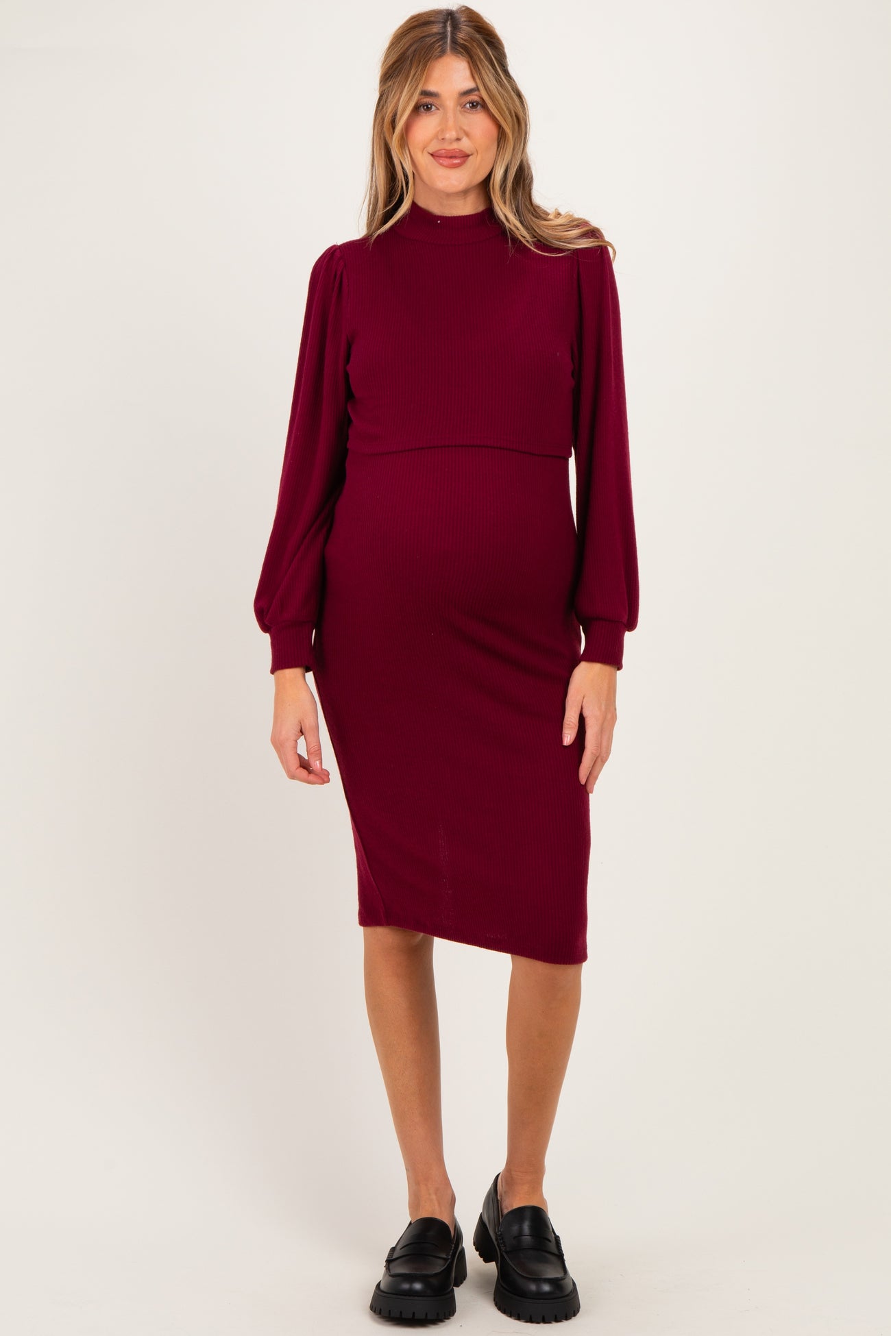 woman wearing a burgundy ribbed maternity dress with long puff sleeves and a fitted silhouette, showing her baby bump