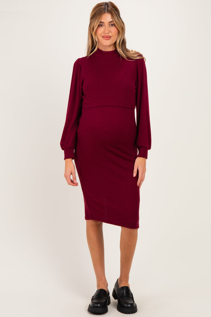 woman wearing a burgundy ribbed maternity dress with long puff sleeves and a fitted silhouette, showing her baby bump