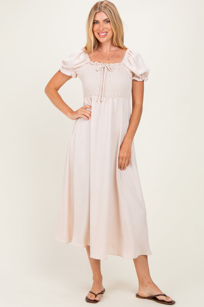 woman wearing a light pink puff sleeve midi dress with a smocked bodice and a tie detail at the neckline