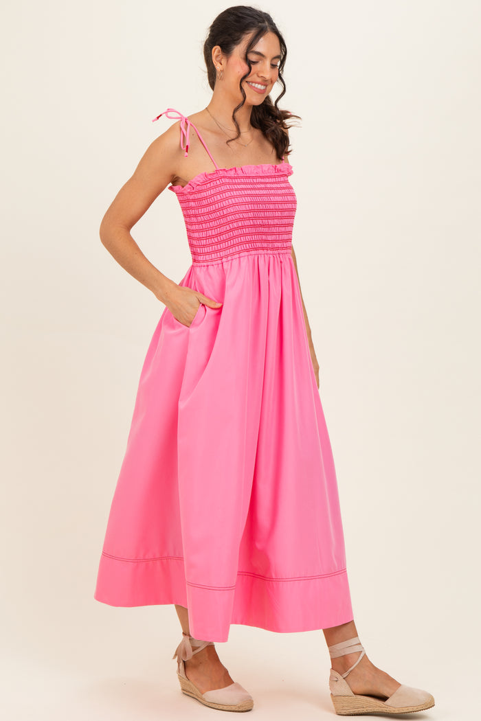 woman wearing a bright pink maxi dress with smocked bodice and tie straps, featuring side pockets and a flowy skirt