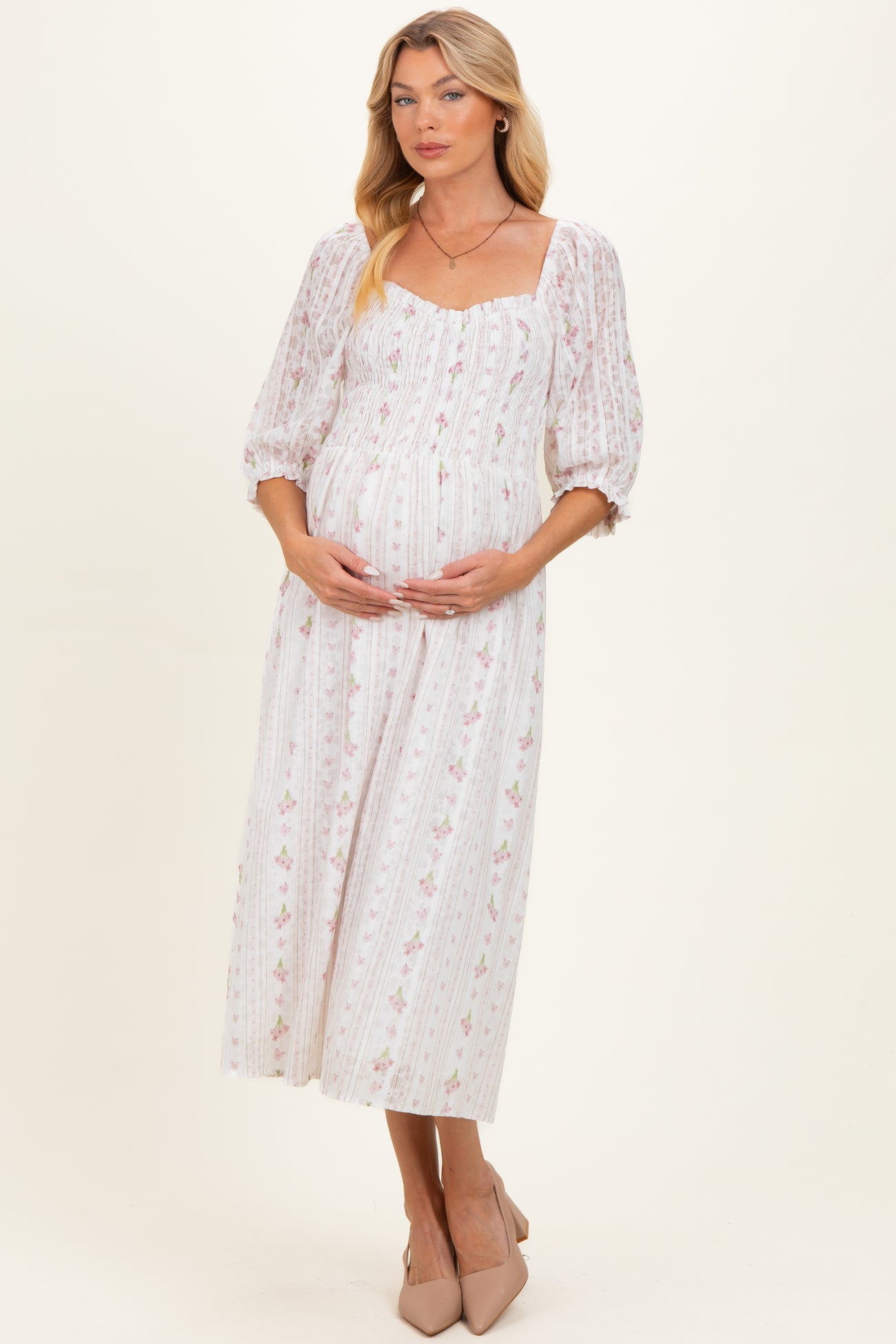 woman wearing a white floral maternity dress with puff sleeves and a square neckline, holding her baby bump