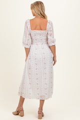 woman wearing a white floral print maternity dress with smocked bodice and puff sleeves, baby bump visible