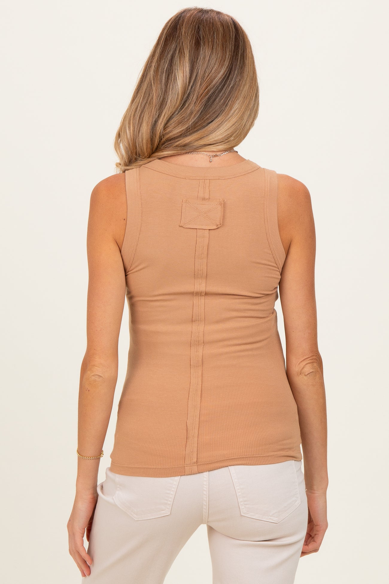 woman wearing a tan sleeveless maternity top with a back seam detail and styled with light-colored pants