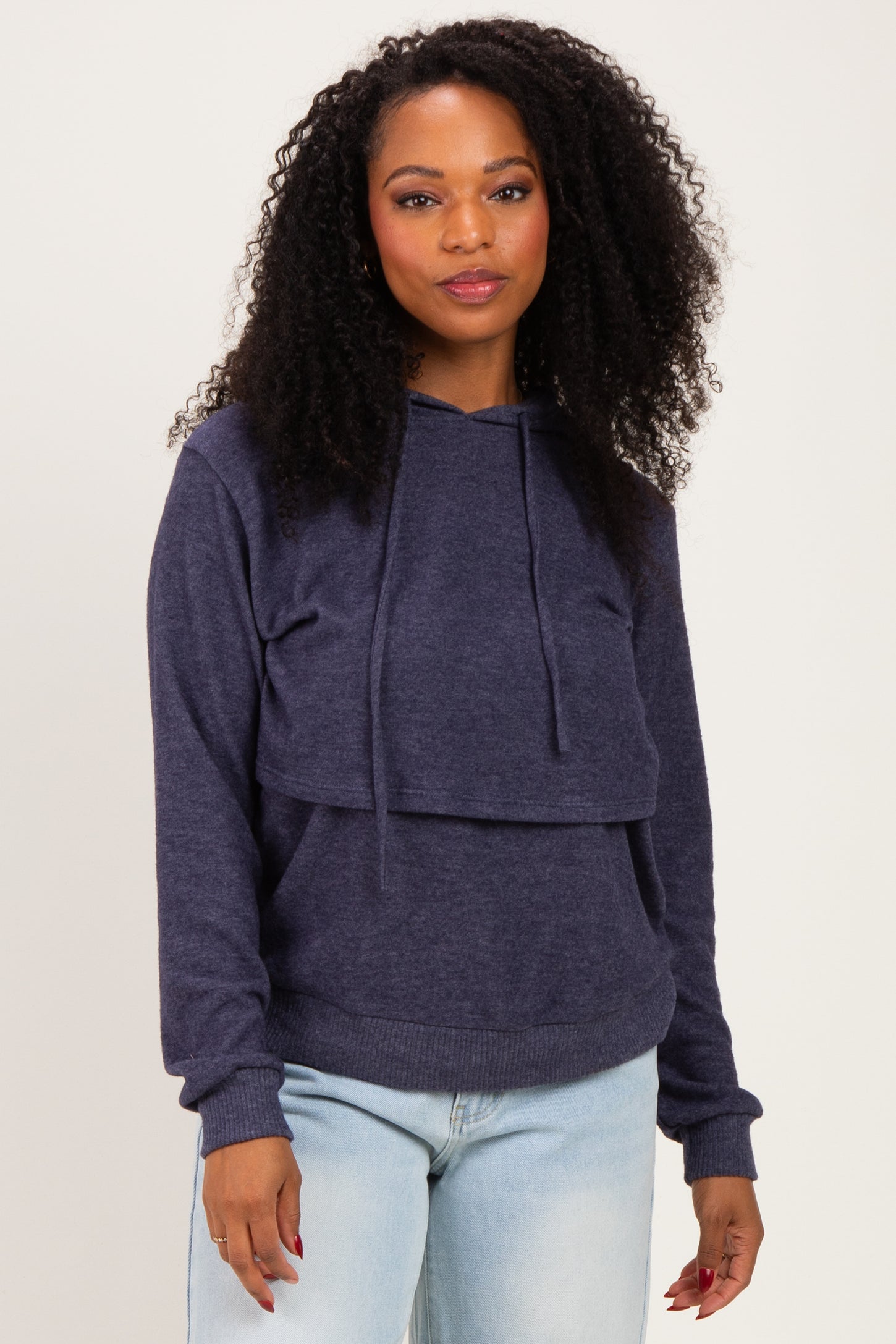 woman wearing a navy blue hooded sweatshirt with a layered look and long sleeves, standing with a slight smile