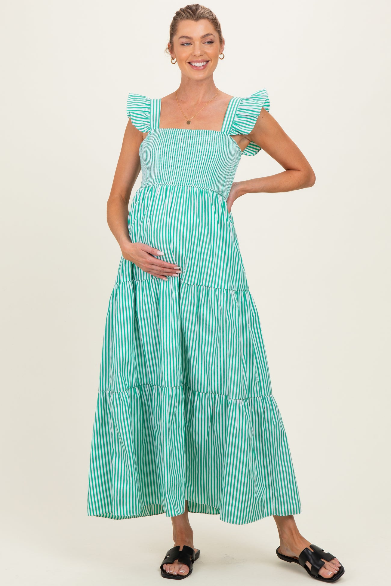 woman wearing a green and white striped maternity maxi dress with ruffle sleeves and holding her baby bump