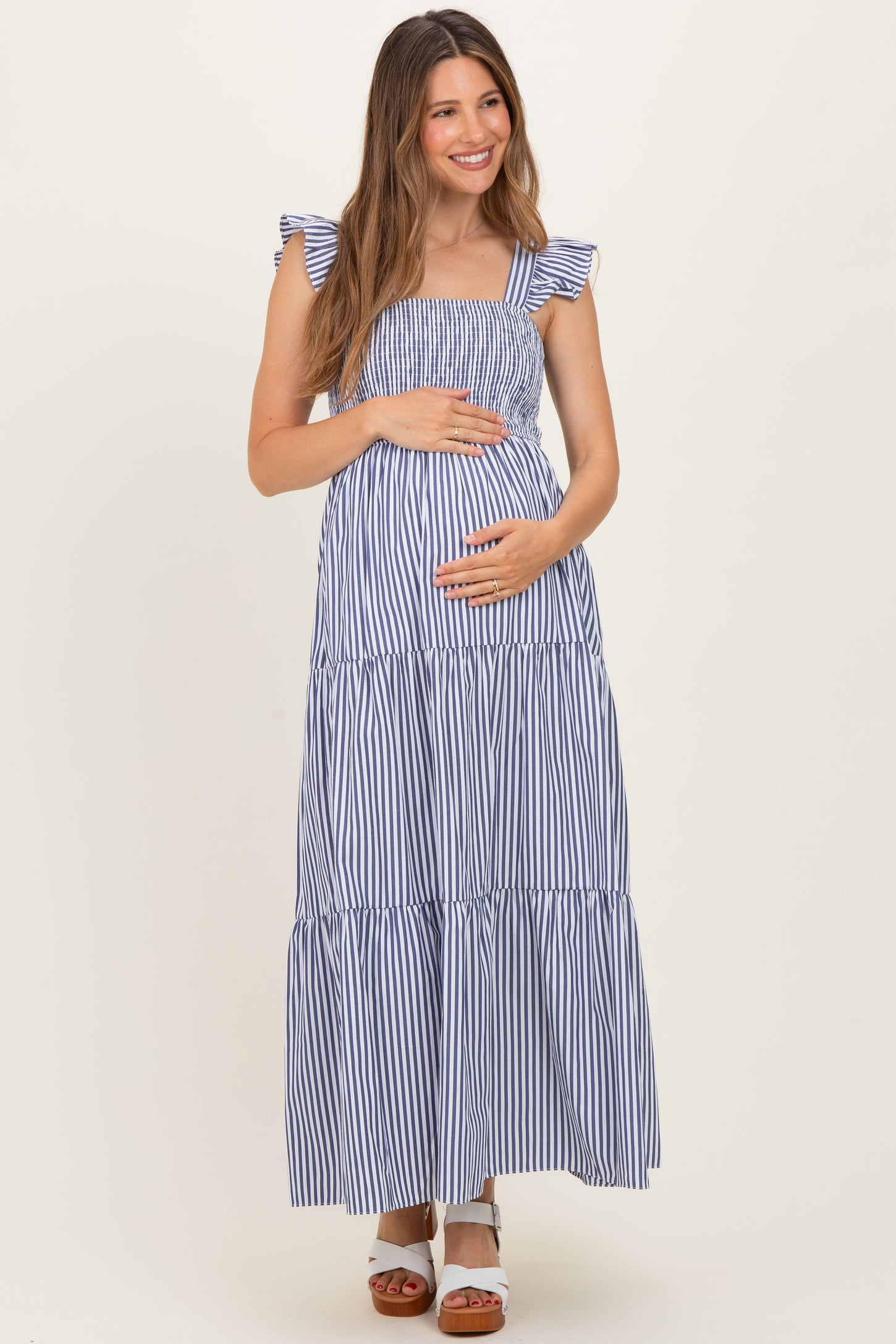 woman wearing a navy and white striped maternity maxi dress with ruffled straps and holding her baby bump