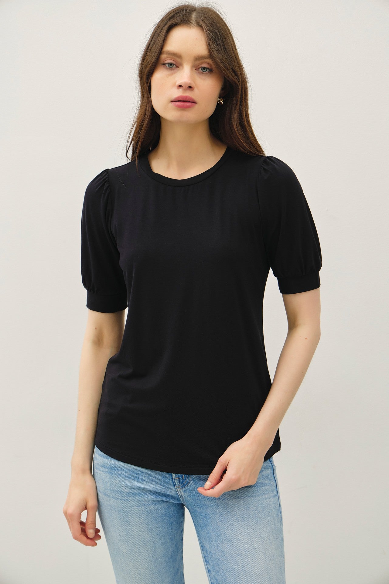 woman wearing a black short sleeve top with puffed sleeves and a relaxed fit, paired with light blue jeans