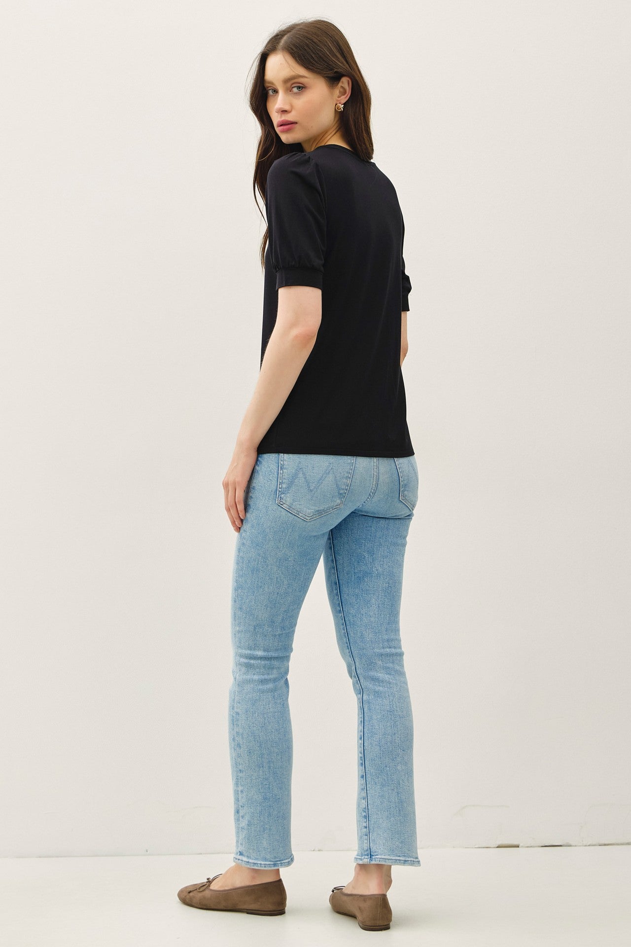 woman wearing a black short sleeve top and light blue fitted jeans, viewed from the back
