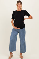 woman wearing a black maternity top with puff sleeves and loose light blue jeans, showing her baby bump