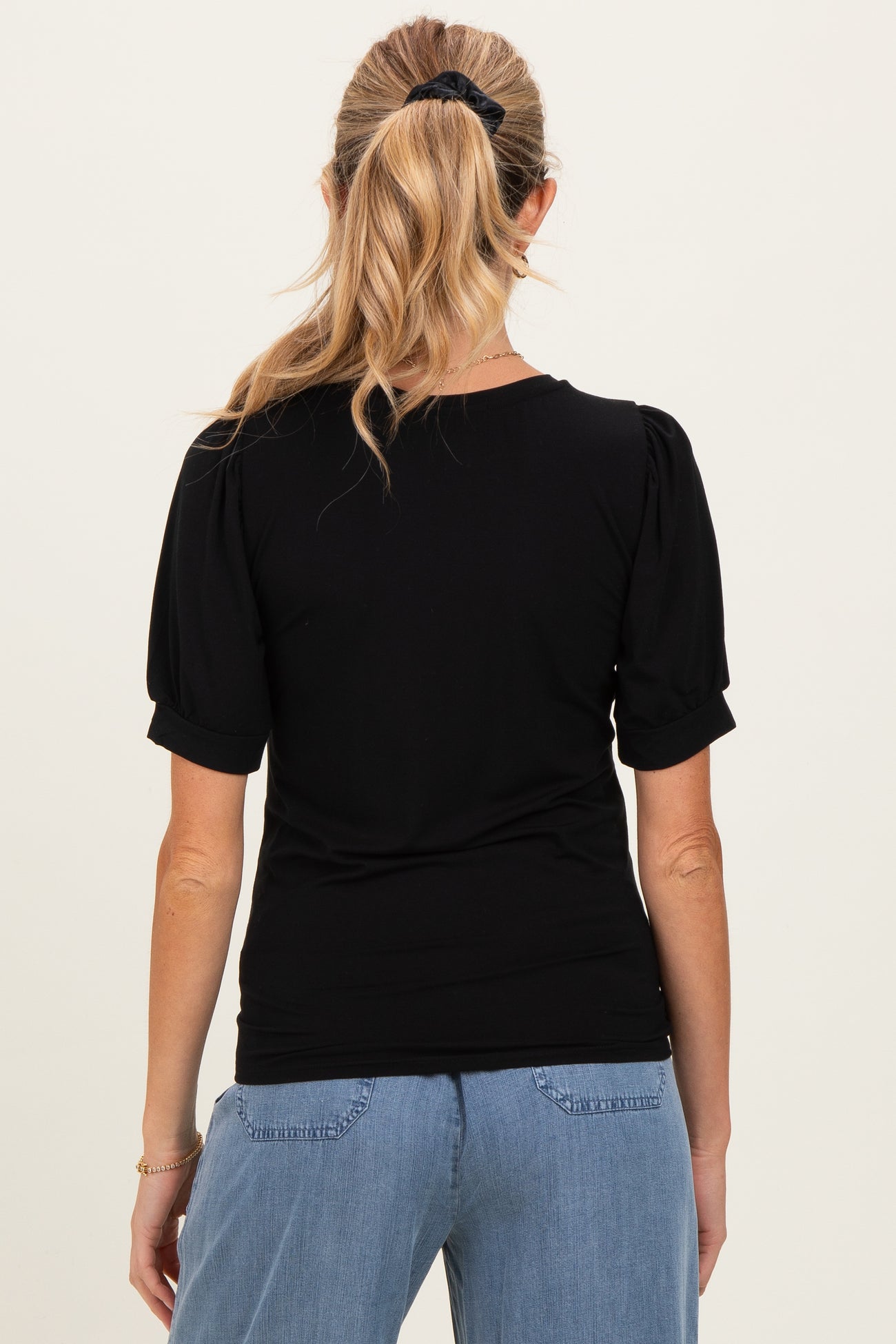 woman wearing a black maternity top with puff sleeves, viewed from the back, paired with light blue jeans