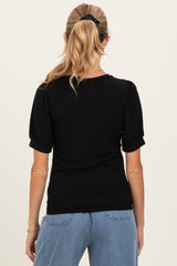 woman wearing a black maternity top with puff sleeves, viewed from the back, paired with light blue jeans