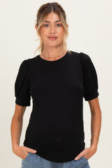 woman wearing a black maternity top with puff sleeves and relaxed fit, smiling and standing with hands in pockets