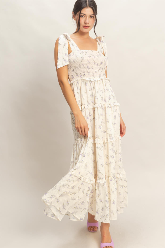 woman wearing a flowy cream maxi dress with lavender floral print and tie shoulder straps.