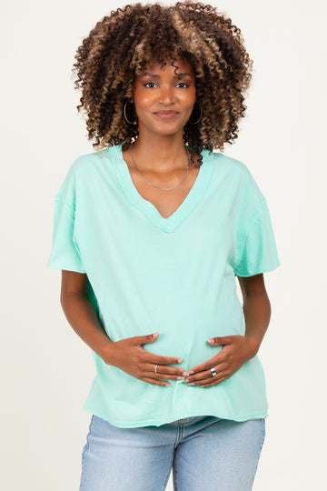 woman wearing a mint green v-neck maternity t-shirt and holding her baby bump