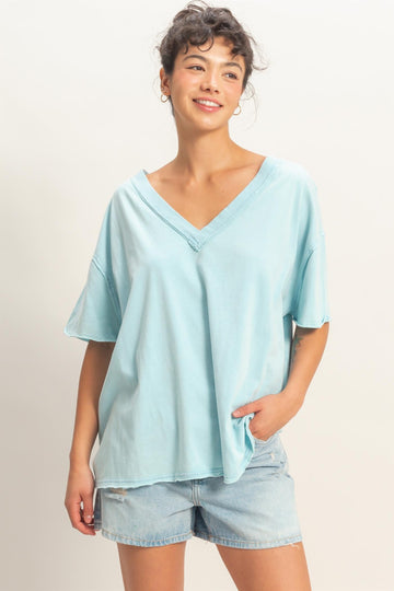 woman wearing a light blue oversized v-neck t-shirt and denim shorts, smiling with one hand in her pocket