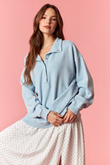 woman wearing a light blue oversized pullover with a collar and front buttons, paired with a white dotted skirt