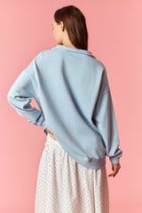 woman wearing a light blue oversized sweater with a scooped neckline and ribbed hem, styled with a white polka dot skirt
