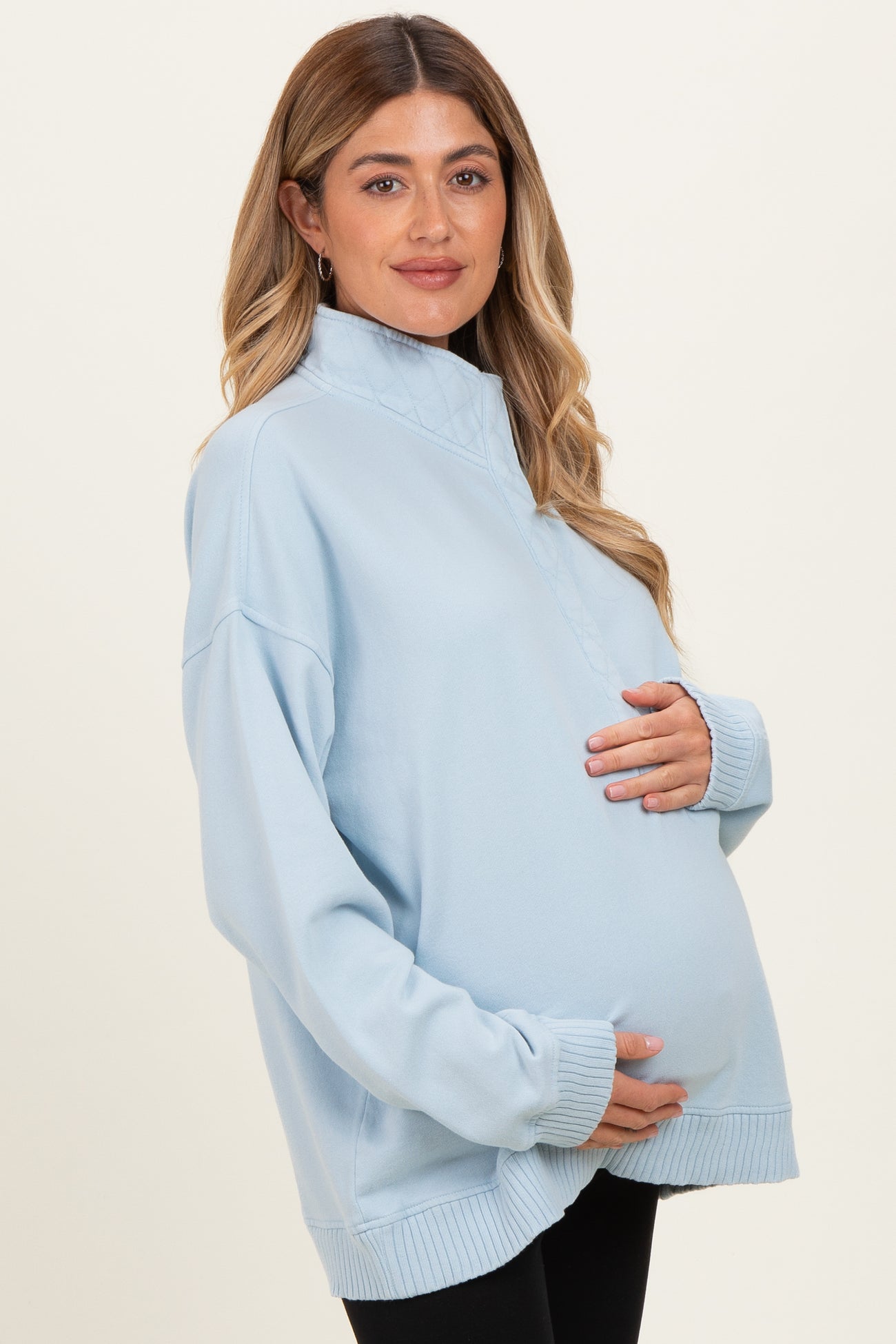 woman wearing a light blue maternity pullover sweatshirts and holding her baby bump