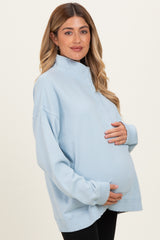 woman wearing a light blue maternity pullover sweatshirts and holding her baby bump