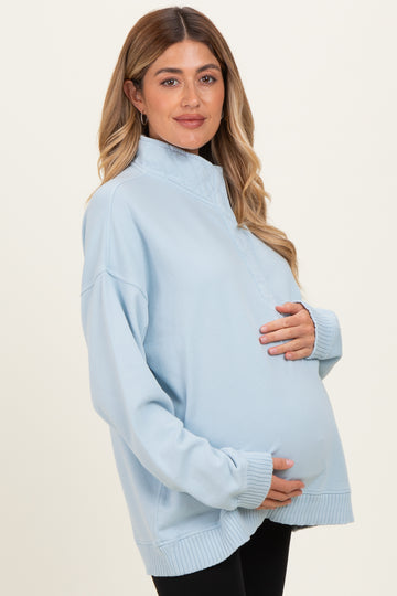 woman wearing a light blue maternity pullover sweatshirts and holding her baby bump