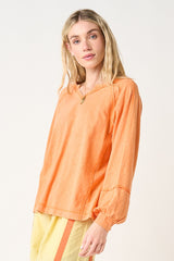 woman wearing an orange long sleeve top with a v-neck and loose fit, paired with yellow pants