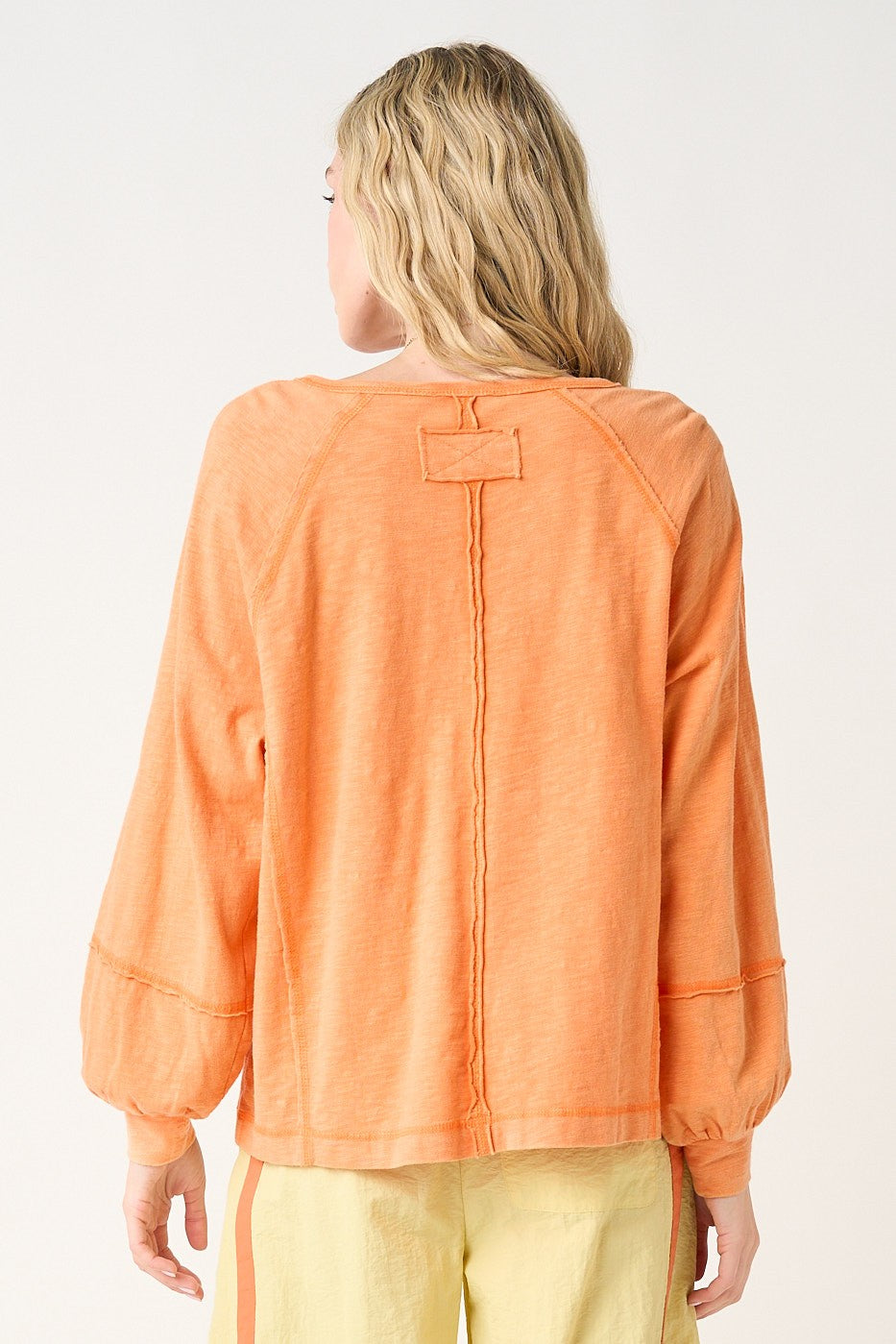 woman wearing an orange long sleeve top with a relaxed fit and pleated details on the sleeves