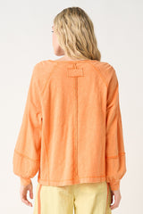 woman wearing an orange long sleeve top with a relaxed fit and pleated details on the sleeves