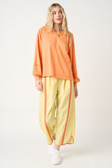 woman wearing an orange long sleeve top with a quarter-zip and yellow wide-leg pants featuring side stripes
