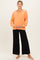 woman wearing an orange maternity top with long sleeves and a v-neck, paired with black wide-leg maternity pants and holding her baby bump
