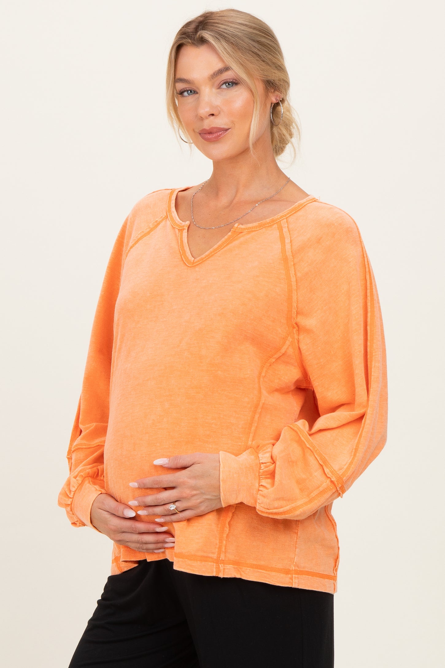 woman wearing an orange long sleeve maternity top with a v-neck and holding her baby bump