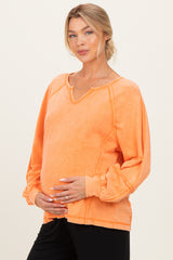 woman wearing an orange long sleeve maternity top with a v-neck and holding her baby bump