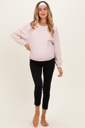 woman wearing a light pink maternity sweatshirt and black maternity leggings, showing her baby bump