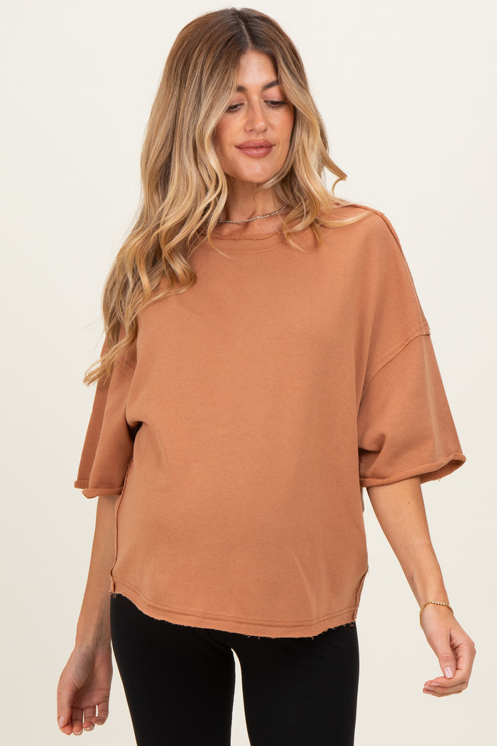 woman wearing a rust-colored oversized maternity top with short sleeves and a visible baby bump