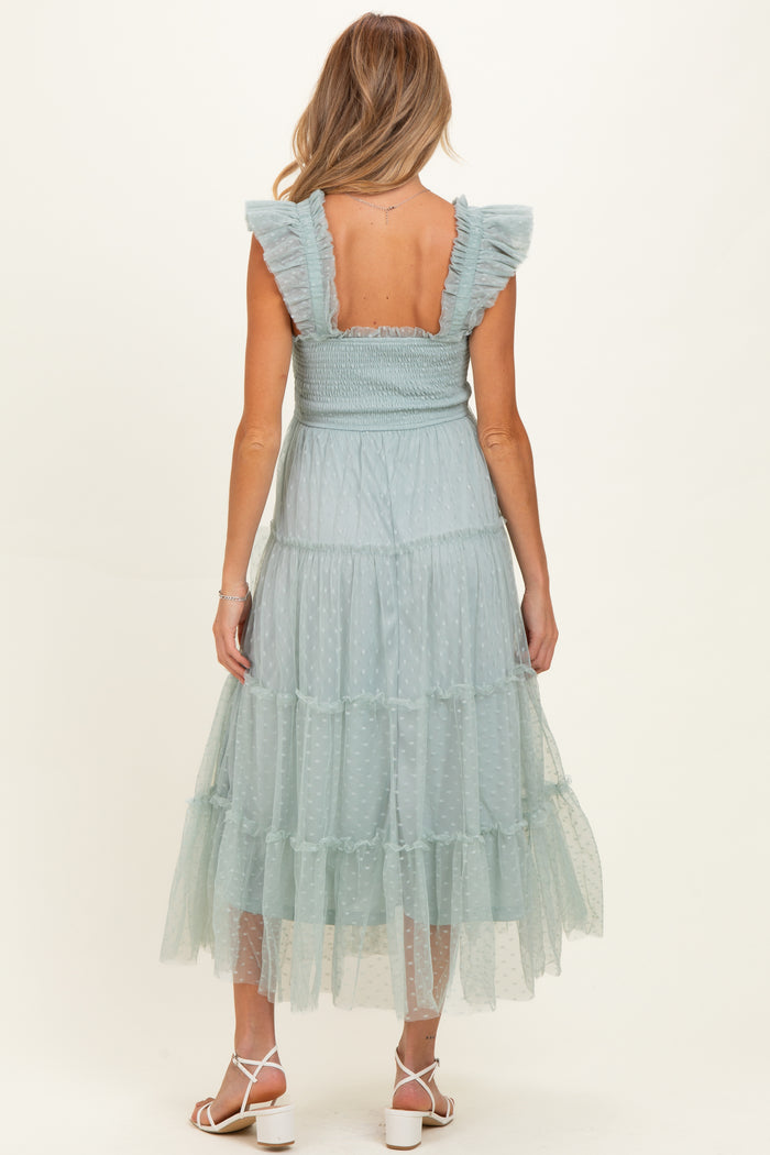 woman wearing a light blue maternity dress with ruffled sleeves and a tiered tulle skirt, showcasing her baby bump