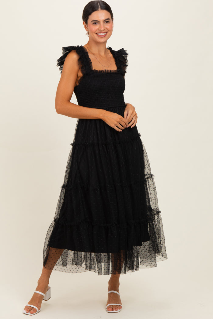 woman wearing a black tiered maxi dress with ruffled straps and sheer overlay, accessorized with white strappy heels