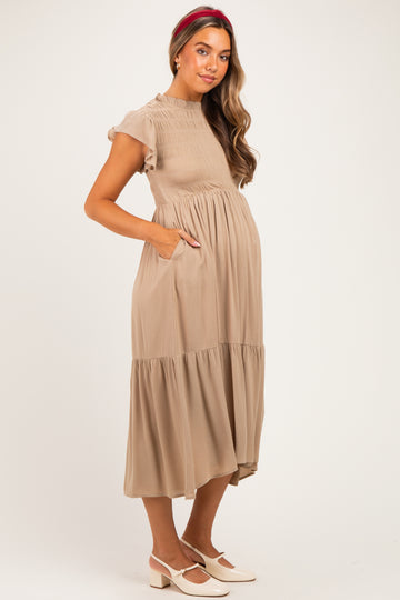 woman wearing a beige maternity dress with short sleeves, smocked bodice, and a tiered skirt, showing her baby bump