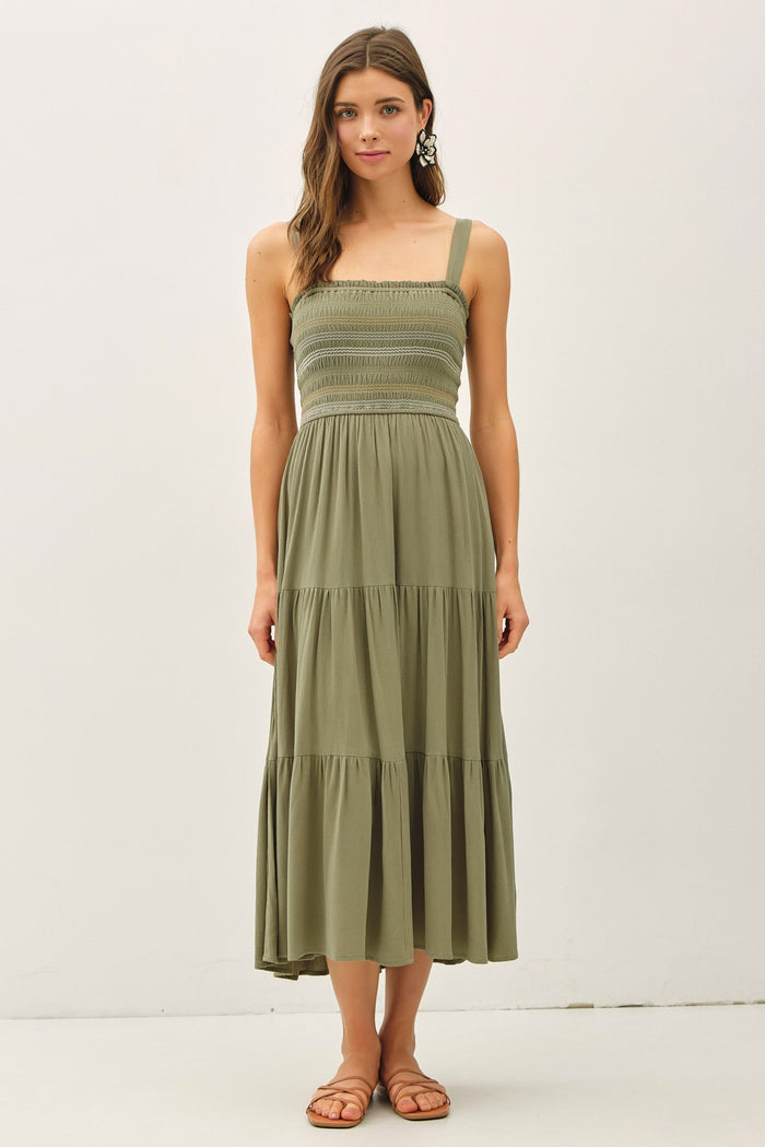 woman wearing an olive green smocked midi dress with adjustable straps and a tiered skirt