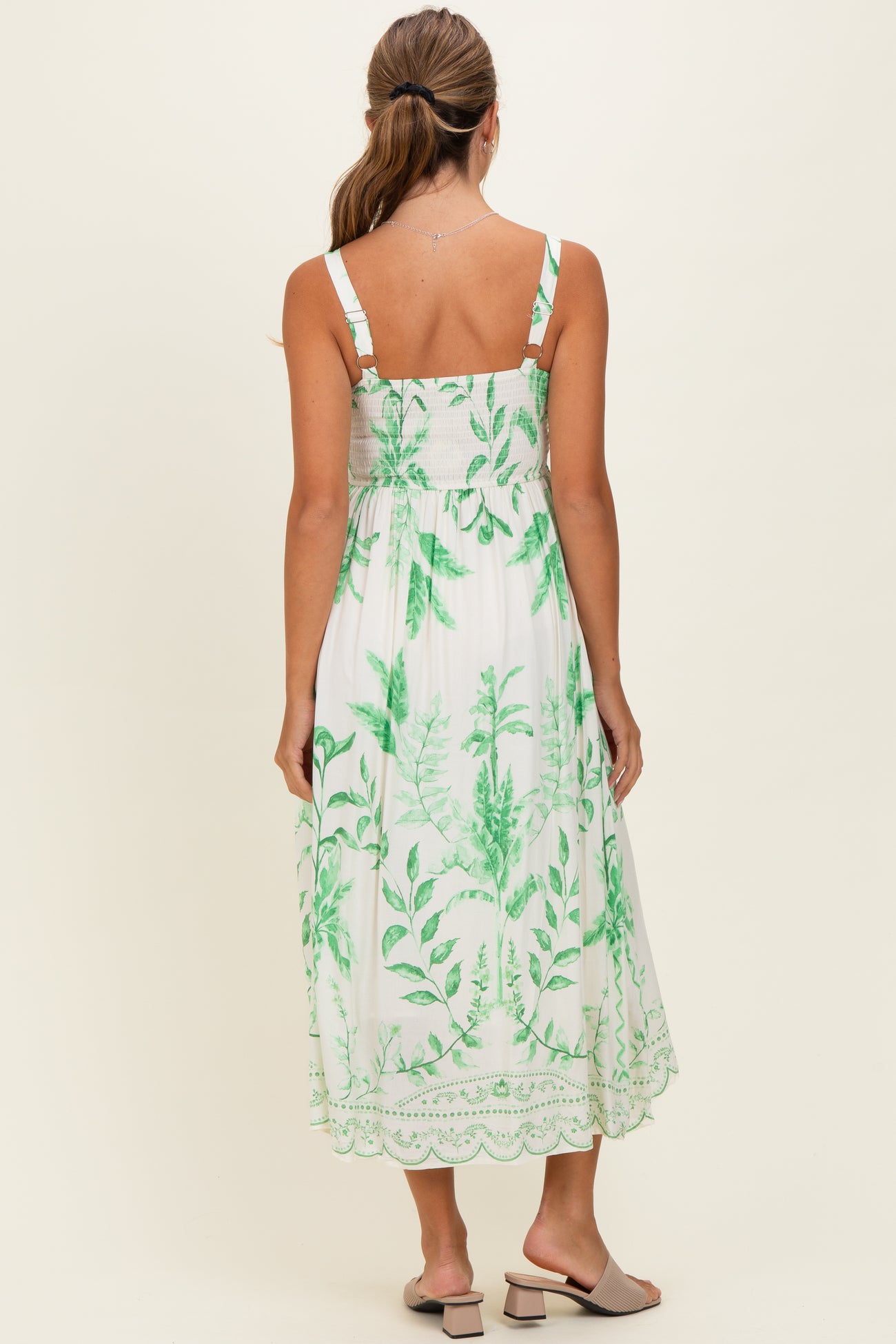 woman wearing a white maxi dress with green leaf prints and adjustable straps, shown from the back