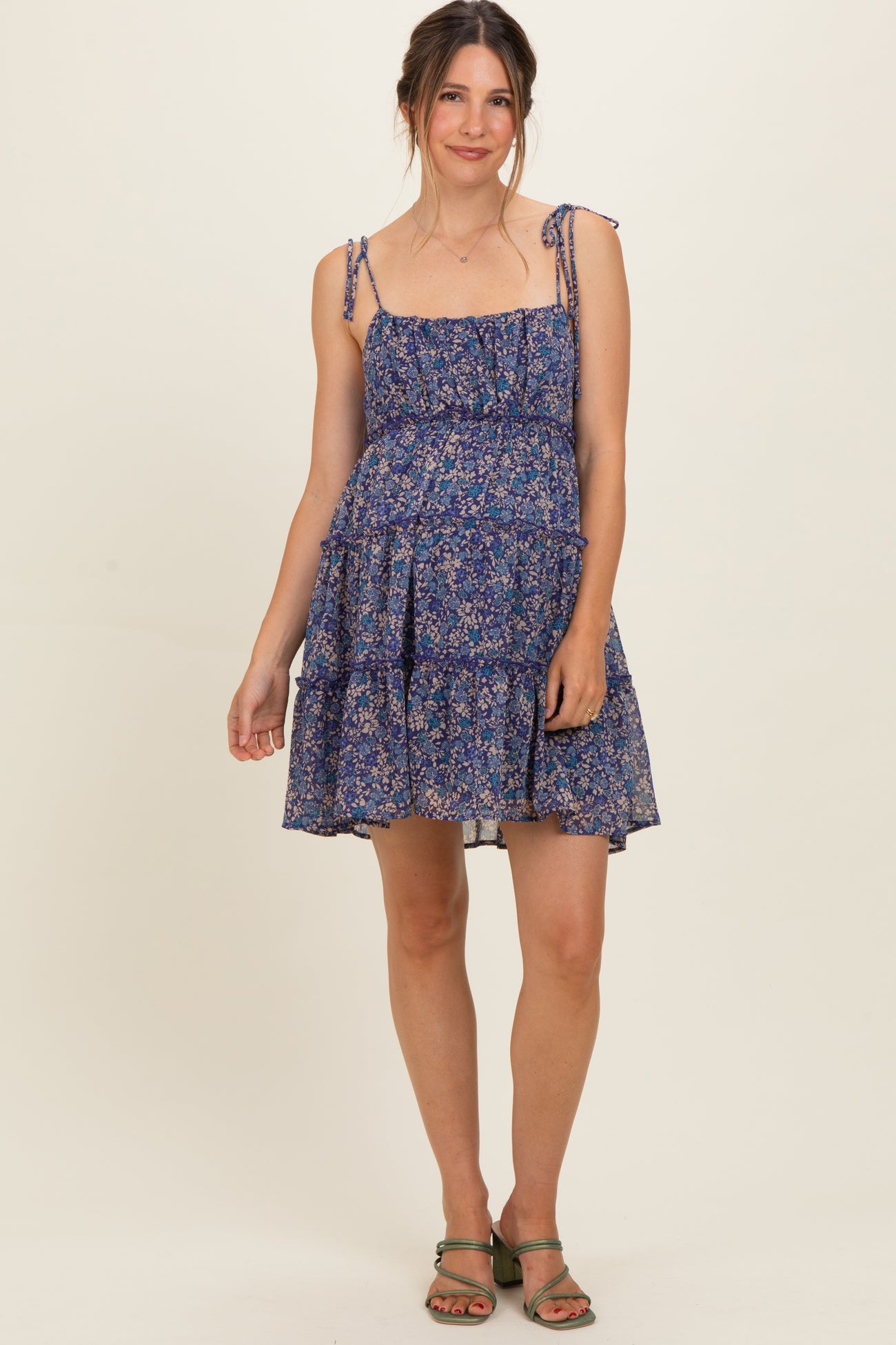 woman wearing a navy floral maternity dress with adjustable straps and tiered skirt, showing her baby bump